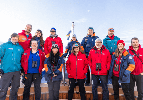 An Deck des Expeditionskreuzfahrtschiffs steht die Expeditionscrew beim Gruppenfoto zusammen